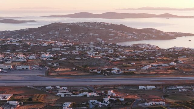 Mykonos Airport runway approaching Aegean Sea with typical Greek villages and white houses on Cyclades islands hills in Greece during amazing sunset golden hour