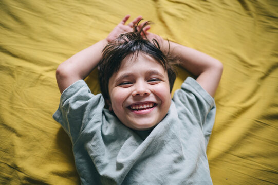 A happy boy enjoys the morning on a yellow bed
