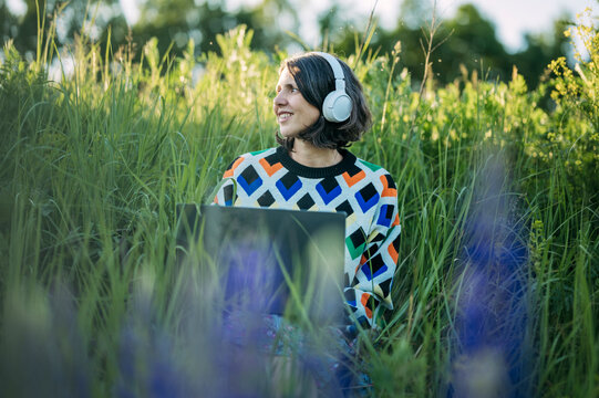 Woman works on laptop with headphone in a green field