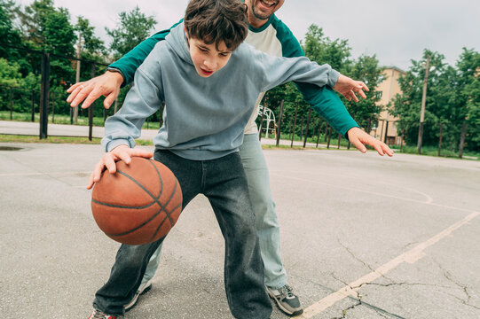 Teenage boy playing basketball outside with his father