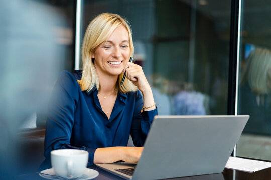 Smiling freelancer using laptop sitting in coffee shop