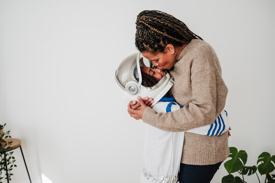 Mother kissing daughter wearing space suit near wall at home