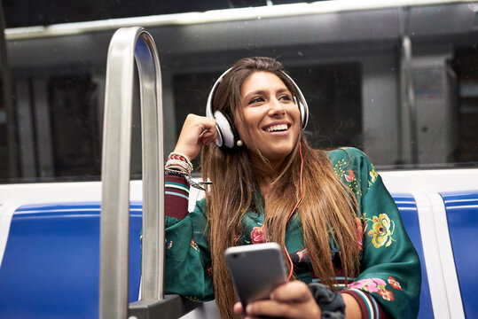 Portrait of happy woman listening music with headphones and smartphone in underground train