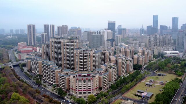 Aerial shot of a dense urban residential area with high-rise buildings, adjacent roads and green spaces, distant city skyline.