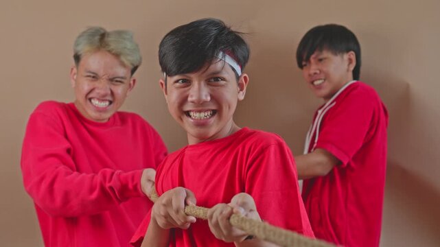 Cheerful Asian boys pulling rope together in studio game competition