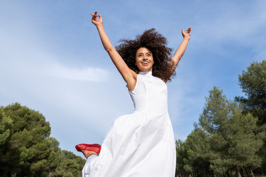 Cheerful model jumping with arms raised in a white dress