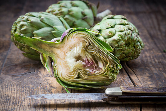 Sliced and whole organic artichokes and kitchen knife on wooden table