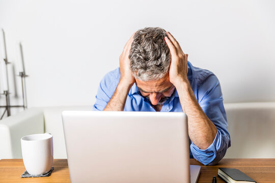 Angry businessman with head in his hands sitting at his home office