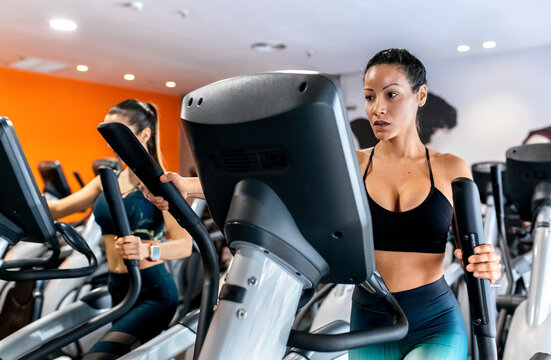 Two women working out in gym using an elliptical trainer