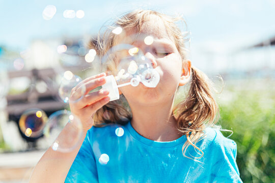Girl blowing bubbles through wand on sunny day