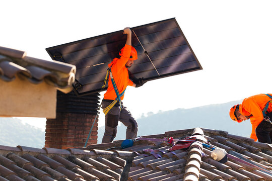 Workers installing solar panel on tiled roof with teamwork and safety