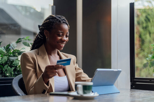 Happy businesswoman holding credit card and using tablet PC at cafe