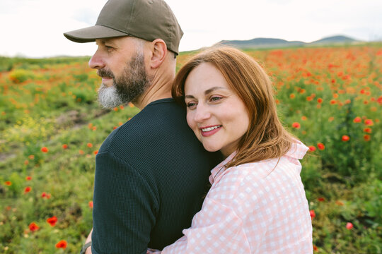 Smiling woman embraces man from behind in a blooming poppy field