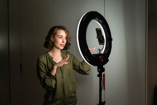 Young female vlogger filming online tutorial through mobile phone at home