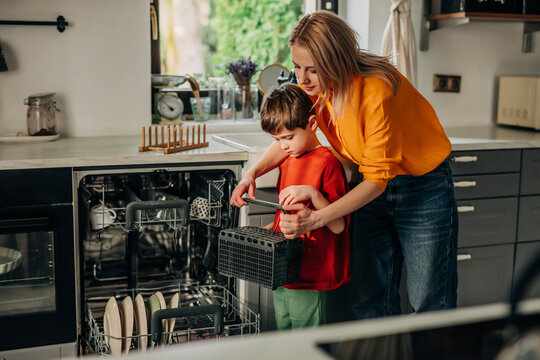 Son helping mother in washing plates using dishwasher at home