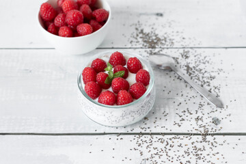 Delicious raspberry chia pudding on a white wooden background.Healthy layered chia seed pudding topped with fresh red raspberries and a mint leaf in a transparent glass bowl. Served on a white wooden  © Margo