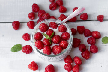 Delicious raspberry chia pudding on a white wooden background.Healthy layered chia seed pudding topped with fresh red raspberries and a mint leaf in a transparent glass bowl. Served on a white wooden  © Margo