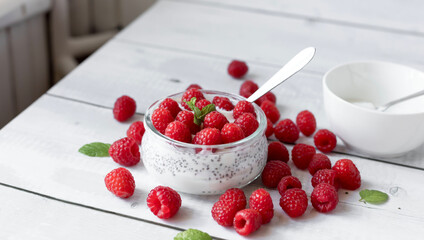 Delicious raspberry chia pudding on a white wooden background.Healthy layered chia seed pudding topped with fresh red raspberries and a mint leaf in a transparent glass bowl. Served on a white wooden  © Margo
