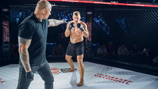 MMA Fighters Fight Start the Fight in the Cage as the Referee Signals the Round. One Fighter Advances With a High Guard, Measuring Distance and Timing.