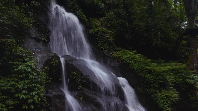 Slow shutter speed shot of a Bali waterfall near Ulu Petanu waterfall, Indonesia. Cinematic. Green vegetation and rocks.
