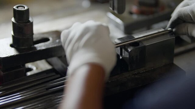 Worker grips metal tool with white glove. Machine presses metal rod into precision holder. Tools align for precise mechanical operation. Use for industrial manufacturing or machinery themes