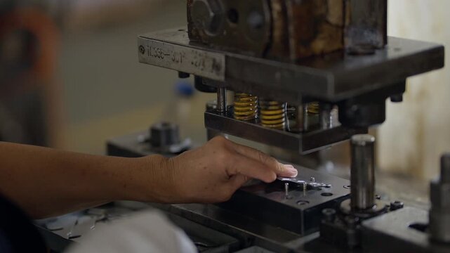 Metal press forms small parts with precision. Hands guide material, showing skilled operation. Workshop environment feels industrious and functional. Ideal for manufacturing, engineering