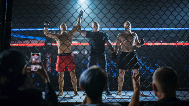 MMA Fighters Await the Official Verdict as the Referee Grips Both Wrists and Raises the Winner&rsquo;s Arm Inside the Cage. Fans Record and Cheer, a Fight for the Champion Title Belt.