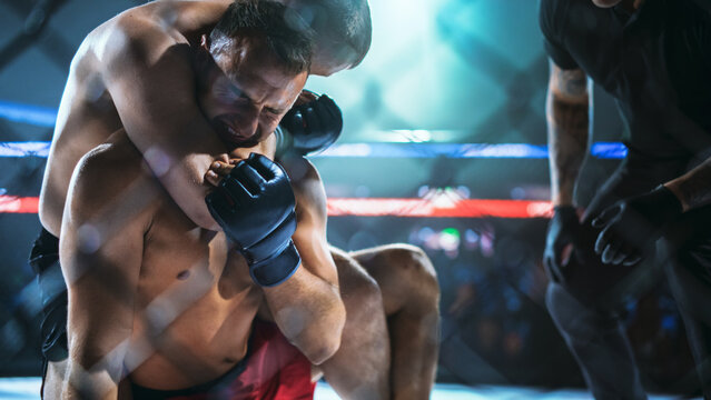 MMA Fighters Grapple in a Tight Submission Fight as One Secures a Rear Naked Choke From Back Control, Forcing a Tap Attempt. Referee Leans in to Judge the Finish, Fight for the Champion Title Belt.