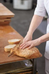 Professional baker slicing fresh rustic bread in a commercial bakery © uv_group
