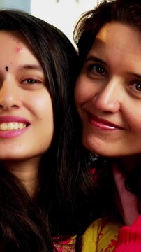 Closeup portrait of a happy Indian Asian pretty young girl in her twenties and her mother in fifties, both looking at the camera while sitting close together on a cozy sofa at home, enjoying their tim