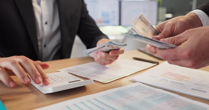 Employees counting cash salary payroll payment in office. Money changes hands over payroll documents and calculator. Suitable for wages topics and finance content. Clear finance concept.