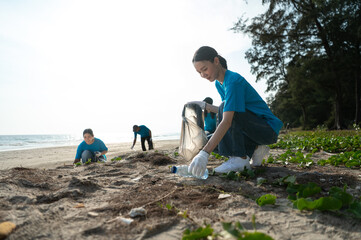Fototapeta premium Group of active Asian volunteers cleaning up plastic waste and garbage on the beach together, focusing on environmental conservation and community teamwork.