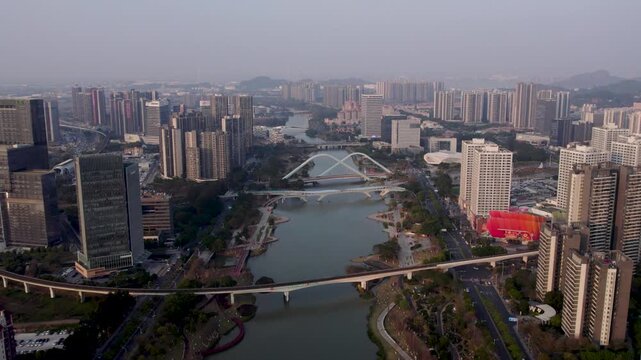 Aerial view of a modern urban area with a river crossing, multiple bridges, and high-rise buildings under a hazy sky.