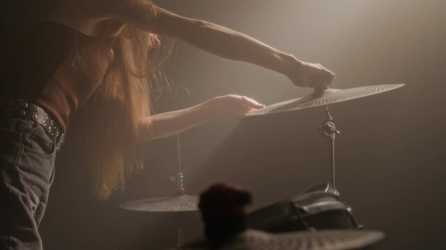 Female musician adjusting cymbal on drum kit and playing drums with drumsticks in music studio. Footage for music school advertisements or musical instrument brand marketing