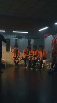 In Cinematic Sports Locker Room, Coach Points to Tactical Diagrams on Flipchart, Briefing Young Athletes on Game Plan and Defensive Strategy. Constructive Criticism, Mental Toughness. Vertical Shot.
