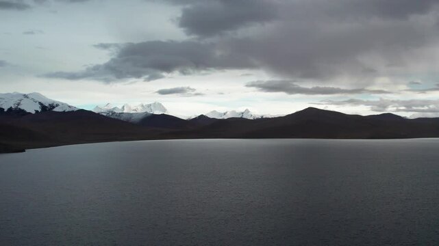 Drone view of beautiful snow covered mountains with moving clouds background in evening, Kula Kangri snow mountain and Pumoyum Co lake in Shannan, Tibet, China. 4K real time footage travel concept.