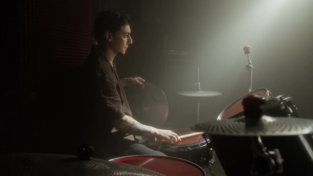 Caucasian young man playing drums and adjusting cymbal in rehearsal studio. Video for music school promotions or instrument brand advertising campaigns