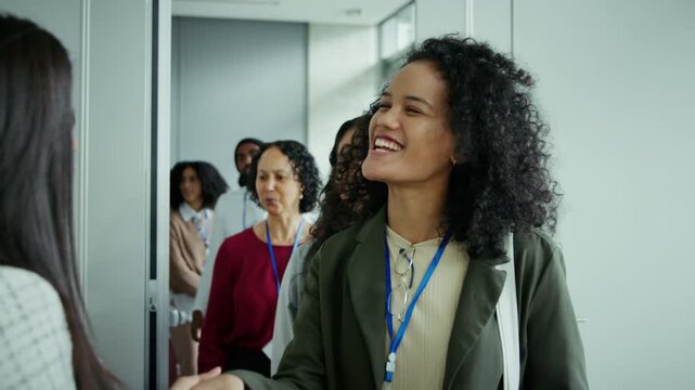 Happy attendees shake hands, smiling warmly as they enter a professional conference event. The group of people are ready to network and engage with others.
