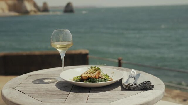 Seaside dining with white wine and grilled fish on a wooden table