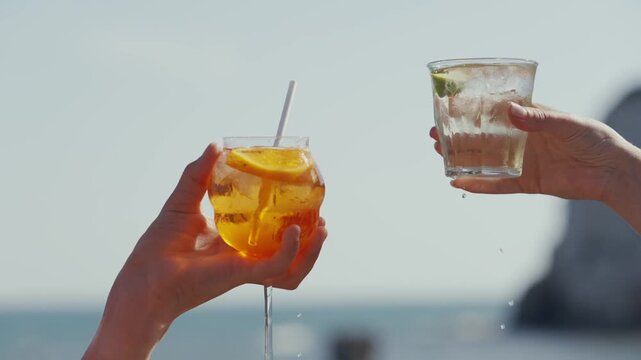 Two hands clink glasses with drinks on a sunny beach vacation