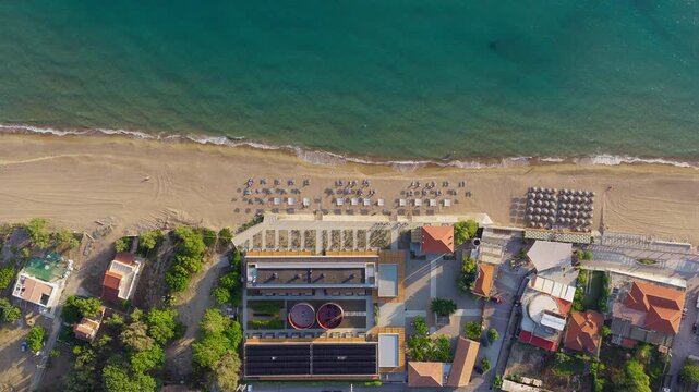 Aerial static shot of Kourouta beachfront bars, luxury restaurants and hotels with sunbeds and natural straw umbrellas, Ilia