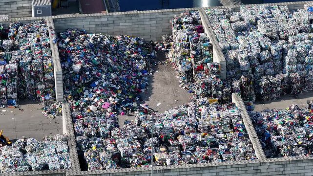 Plastic waste is sorted and processed at a recycling facility. Large piles of plastic materials are visible. The area is organized for efficient recycling operations.