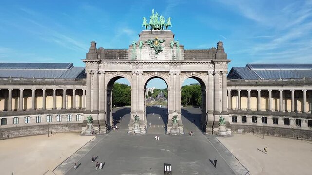 Aerial drone footage slowly flying forward towards the center of the historic Cinquantenaire triumphal arch in Brussels, Belgium, offering a majestic and symmetrical frontal view of the monument