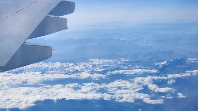 A plane wing is visible against a clear blue sky with scattered clouds below. 