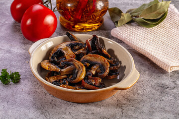 Fototapeta premium Appetizing sauteed mushrooms in a ceramic bowl with fresh ingredients on a stone table