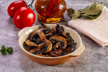 Fototapeta premium Rustic bowl of cooked mushrooms with fresh tomatoes, herbs, and seasoned oil on a stone table