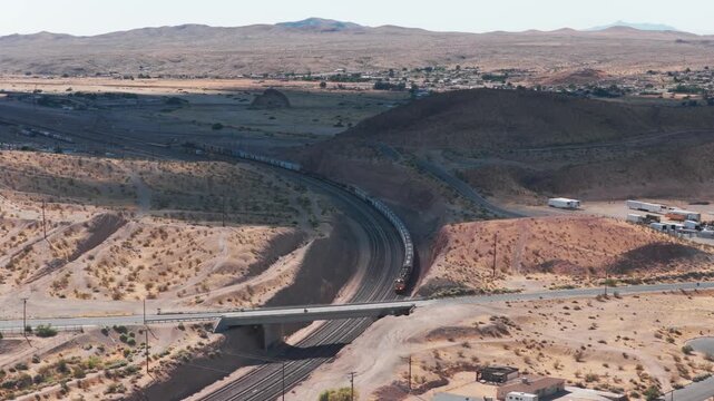 Aerial descending close-up shot of a moving freight train cutting through the desert in Barstow, California. 4K