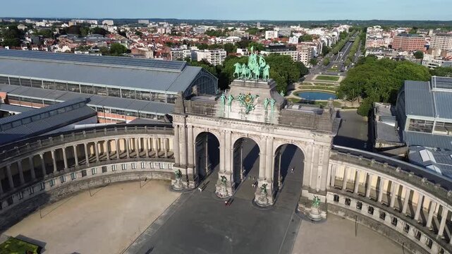 Aerial drone footage showing a slow rotation around the iconic Cinquantenaire triumphal arch and its bronze quadriga statue in Brussels, Belgium, revealing the historic colonnade and the city skyline 