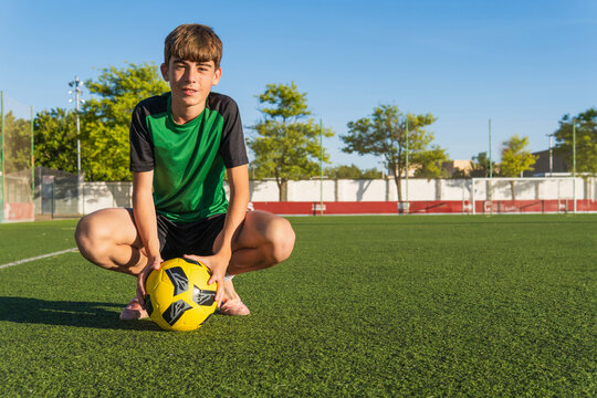 Young football player crouching with ball on soccer field