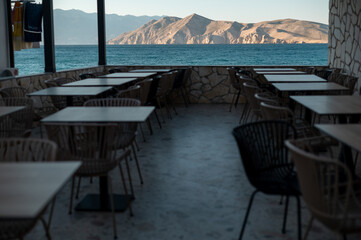 Fototapeta premium Empty seaside restaurant terrace with tables and chairs overlooking the ocean and mountains